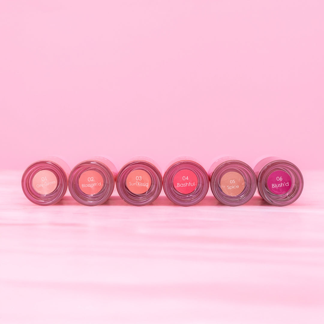 Beaut. Lip Gloss'd six shades in clear tubes with pink caps displayed bottom-up showing shade names: 01 Girly Guava, 02 Blossom'd, 03 Sun Kiss'd, 04 Bashful, 05 Spice, and 06 Blush'd on pink background