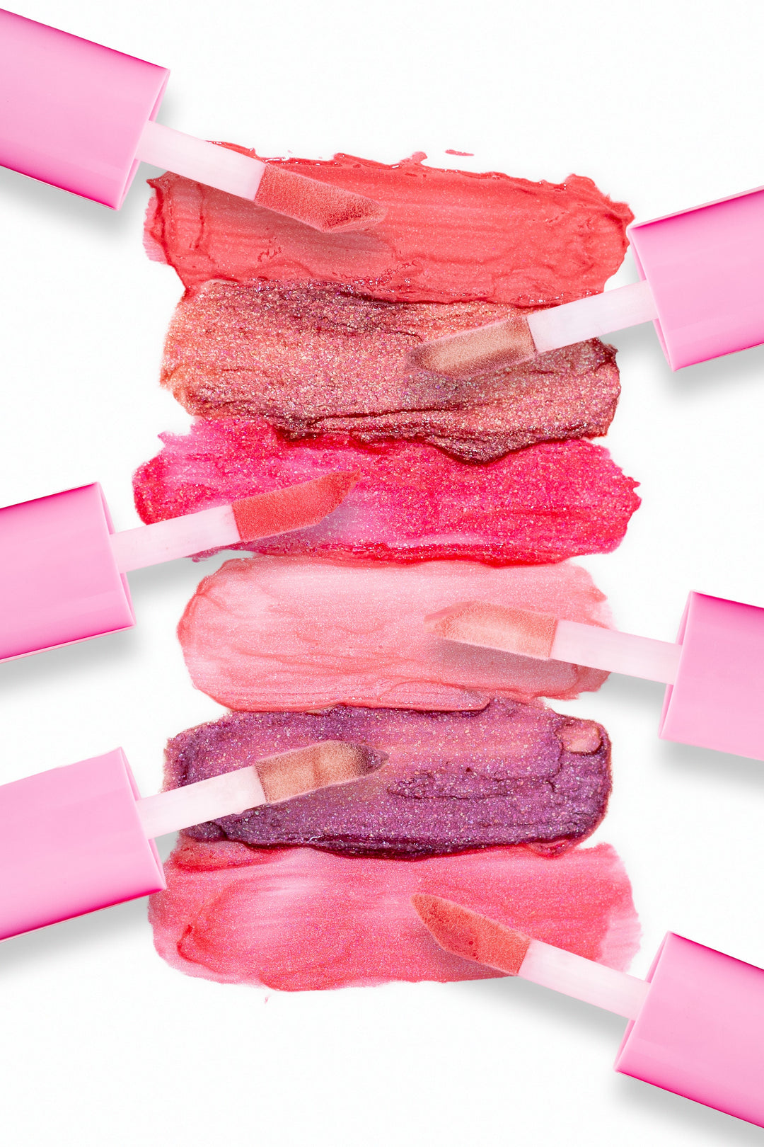 Beaut. Lip Gloss'd color swatches in six shades with pink-capped applicators showing coral red, rose gold glitter, hot pink, blush, purple glitter, and pink on white background