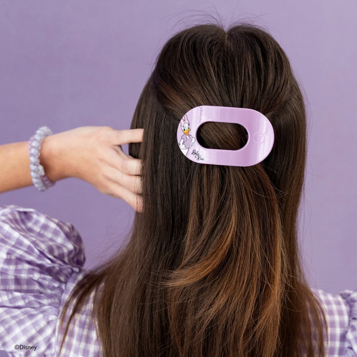 Disney x Teleties Daisy Duck small flat round hair clip in lavender being placed in half-up style on brunette hair by model in plaid top against lavender background