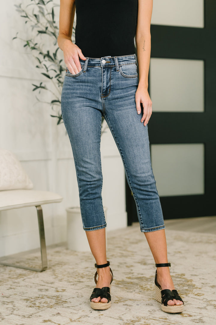 Front cropped view of model wearing Judy Blue medium wash high-rise tummy control rhinestone letter-print cropped straight jeans with hand in pocket, styled with a black tank top and black espadrille wedge sandals.