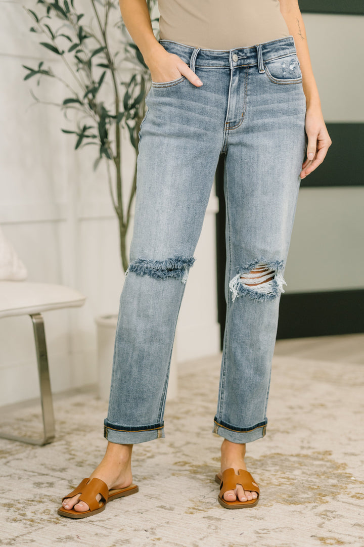 Front view of light wash distressed straight-leg jeans with frayed double knee cutouts and cuffed hem in regular size paired with tan slide sandals
