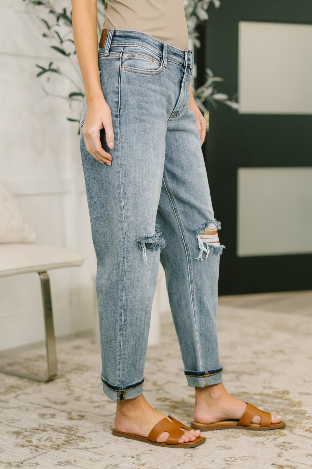 Side view of light wash distressed straight-leg jeans with frayed knee cutouts and cuffed hem in regular size paired with tan slide sandals
