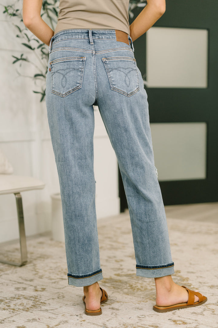 Back full-length view of light wash distressed straight-leg jeans with heart-stitched back pockets and cuffed hem in regular size paired with tan slide sandals