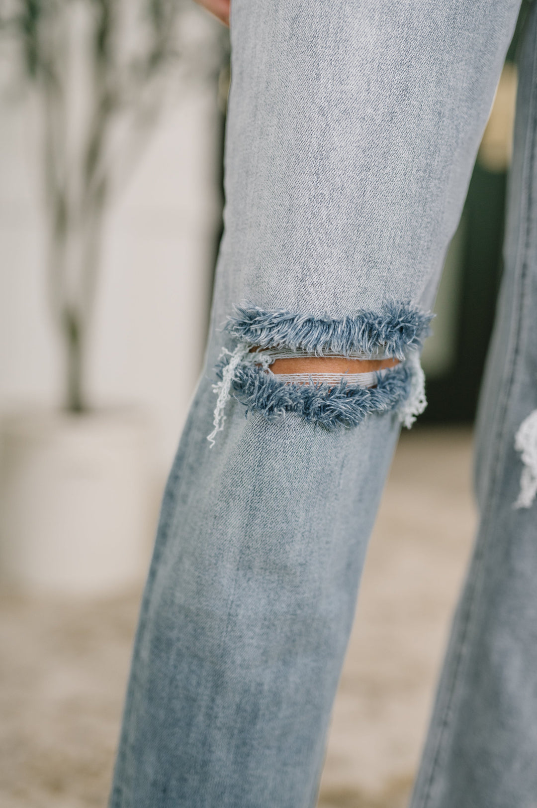Close-up of light wash straight-leg jeans showing frayed open knee cutout detail in regular size
