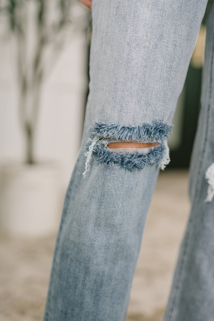 Close-up of light wash straight-leg jeans showing frayed open knee cutout detail in regular size

