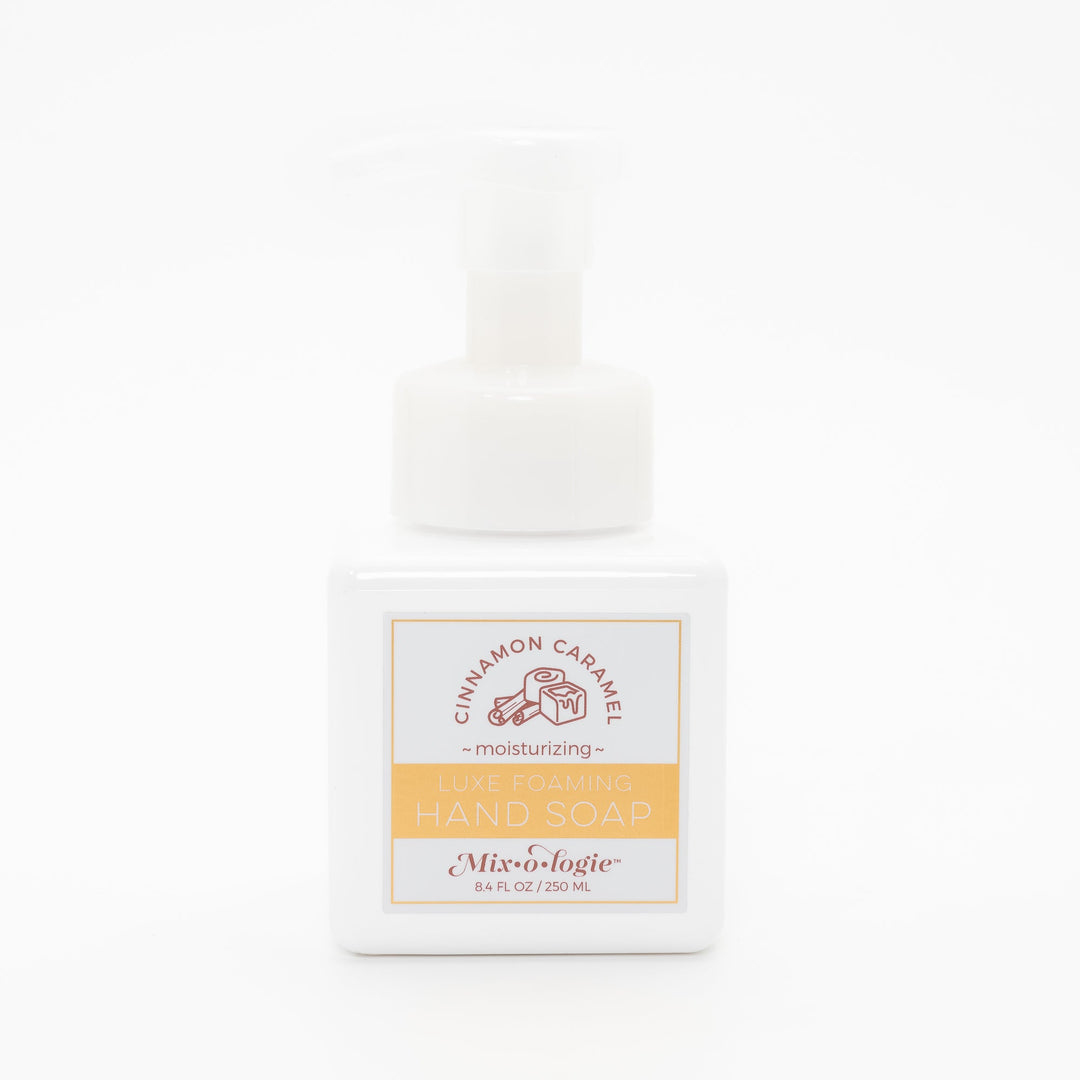 Mixologie Luxe Foaming Hand Soap in Cinnamon Caramel, 8.4 fl oz, white square pump bottle with gold-bordered label and brown cinnamon roll and caramel cube illustration on white background
