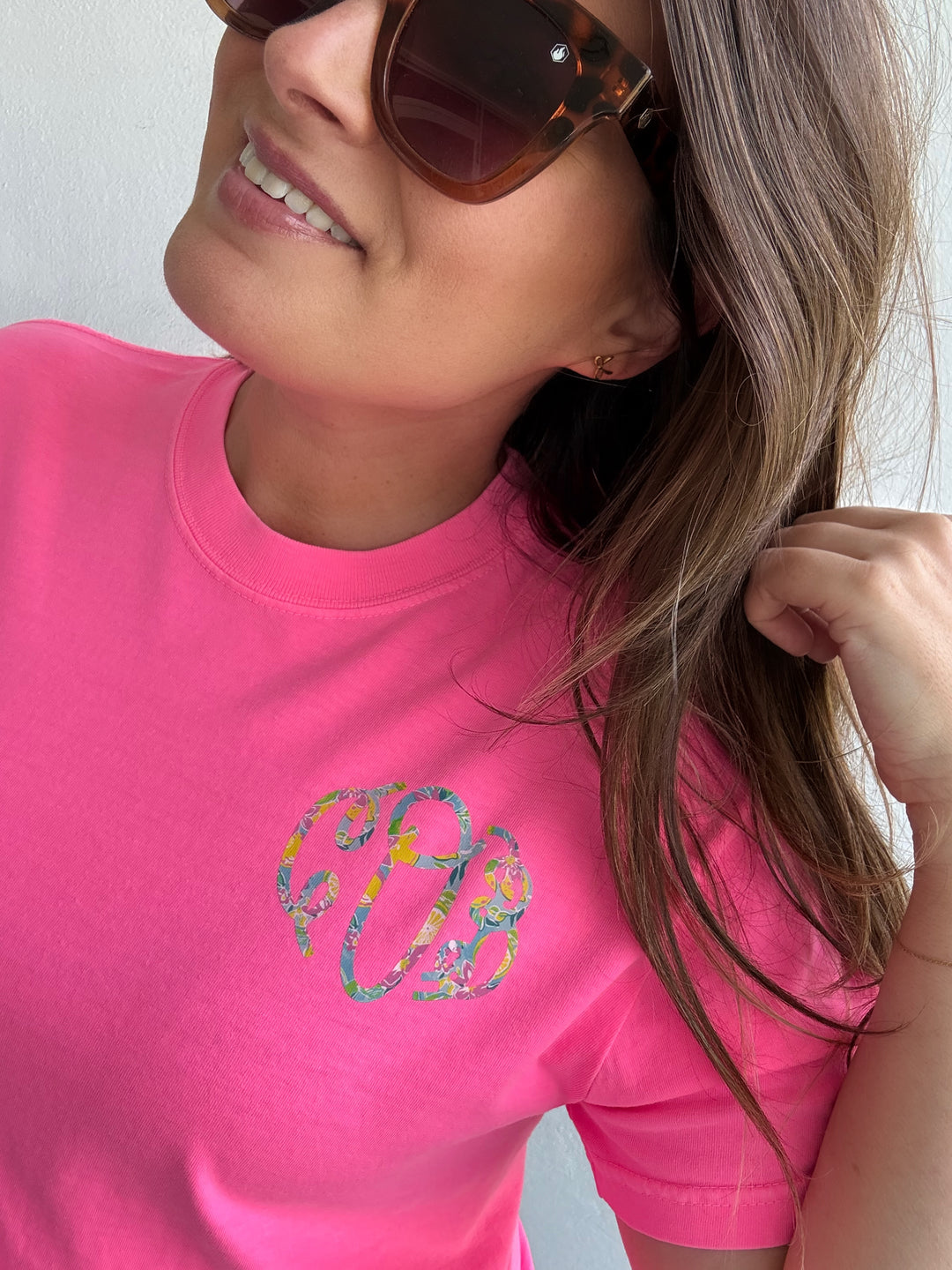 Woman wearing a hot pink t-shirt with a floral monogram graphic on the left chest
