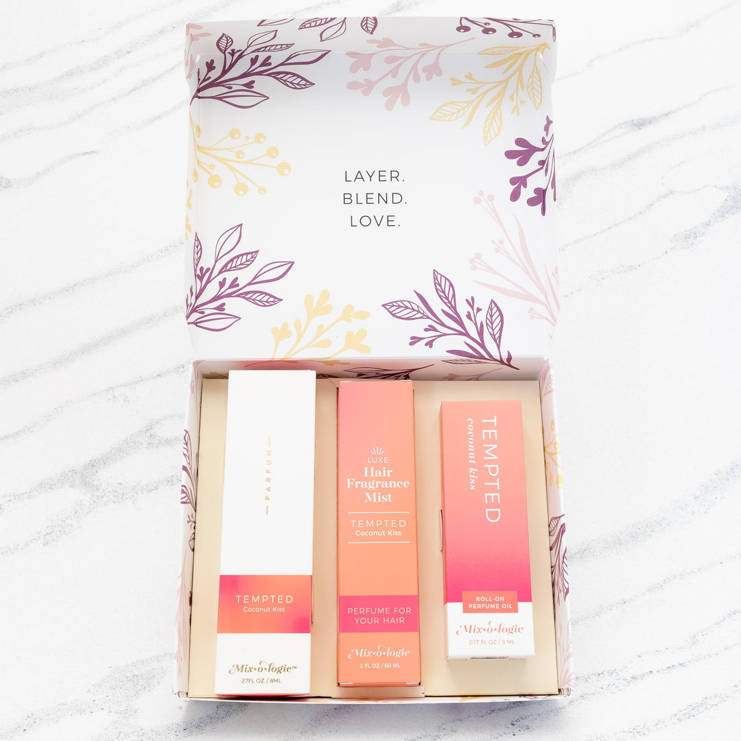 Mixologie Party of Three Gift Set in Tempted Coconut Kiss open box showing parfum spray, Luxe Hair Fragrance Mist, and roll-on perfume oil in coral pink gradient packaging