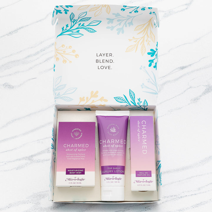 Mixologie Charmed Shot of Spice gift set trio open box showing Moisturizing Body Mist, Top Shelf Luxury Lotion, and Roll-On Perfume Oil in purple gradient packaging