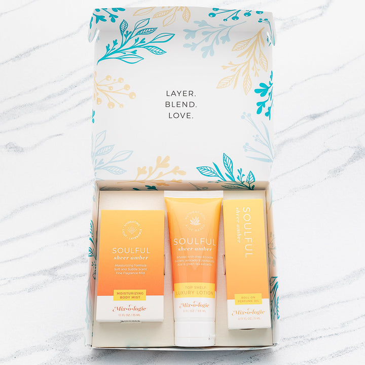 Mixologie Soulful Sheer Amber gift set trio open box showing Moisturizing Body Mist, Top Shelf Luxury Lotion, and Roll-On Perfume Oil in orange to yellow gradient packaging