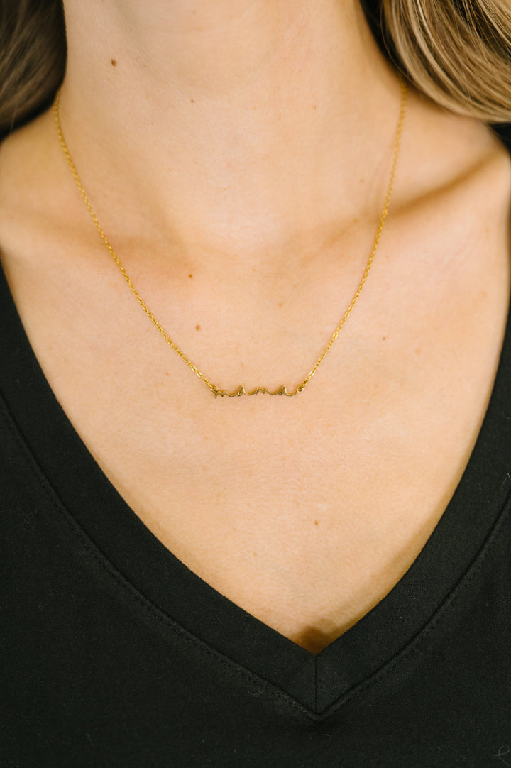 Woman wearing a delicate gold chain necklace with a "mama" script pendant, styled over a black v-neck top