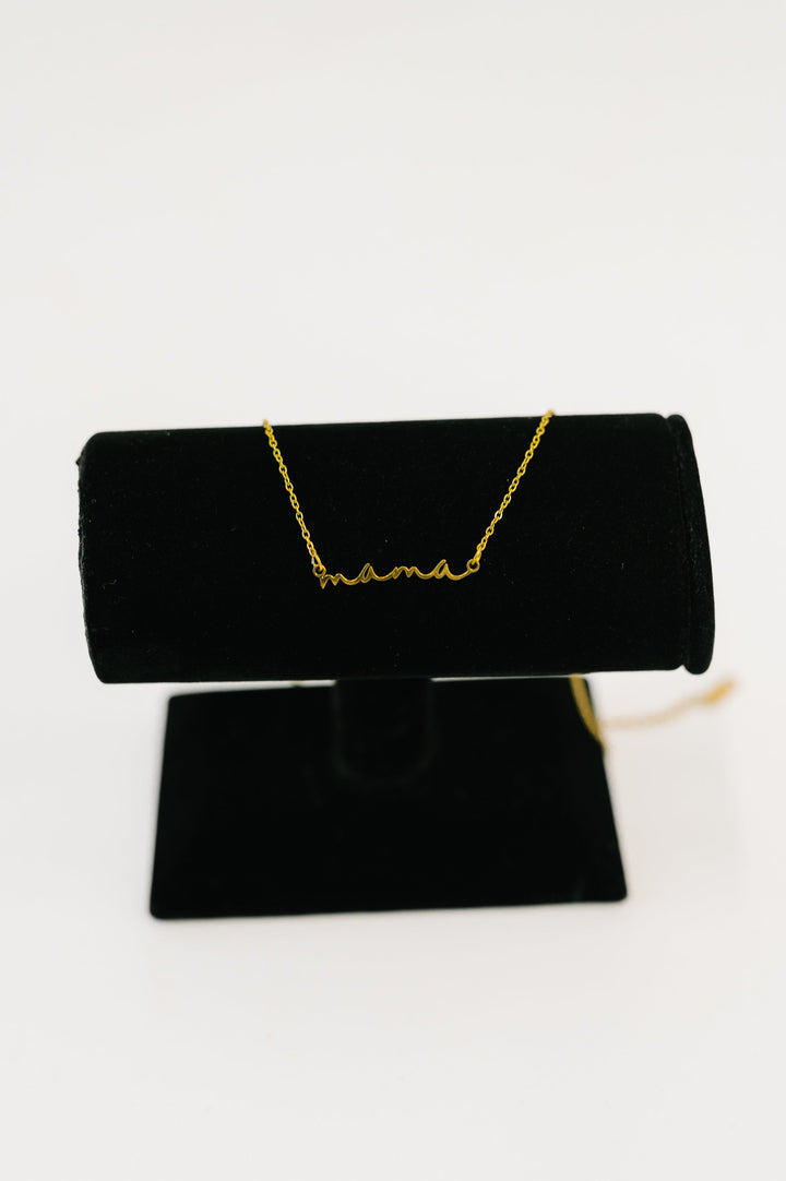 Gold "mama" script necklace displayed on a black jewelry stand against a white background