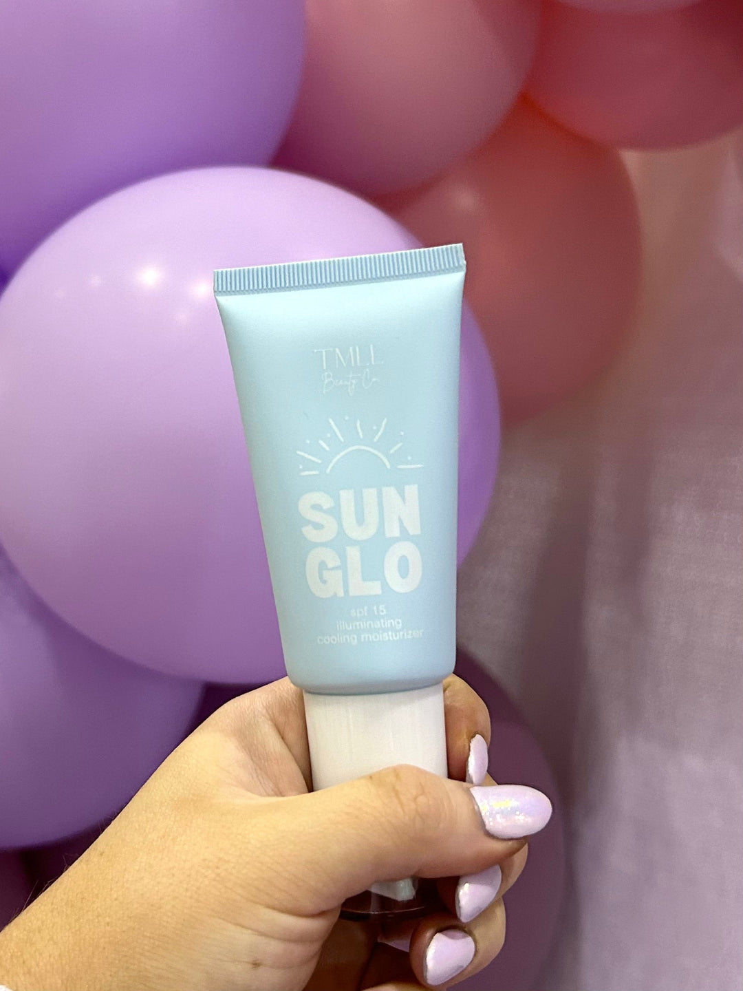 TMLL Beauty Co Sun Glo SPF 15 tinted moisturizer white tube and Sun Glo cooling moisturizer light blue tube with product swatches on pink surface