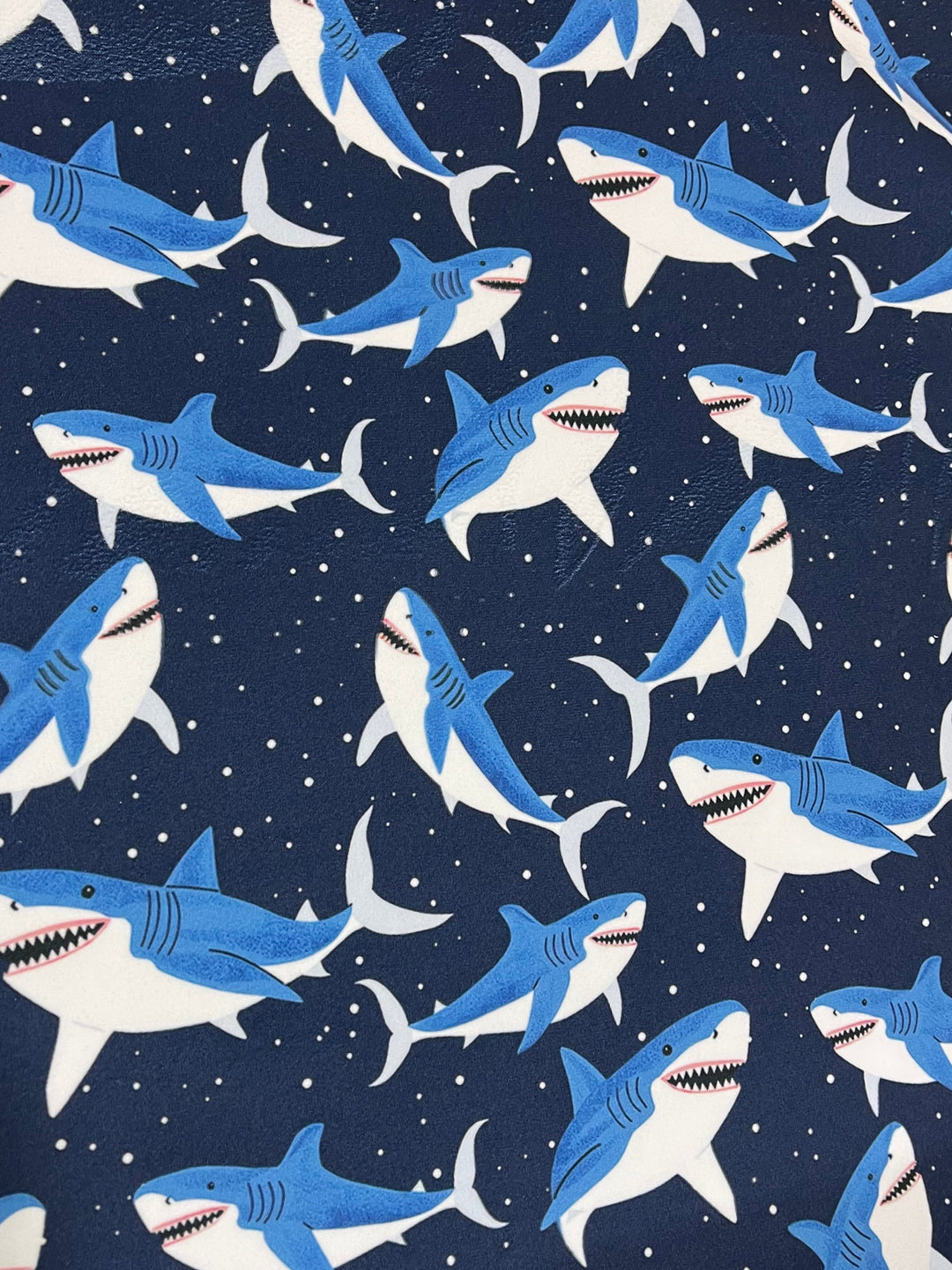 Navy blue shark print fabric with blue and white cartoon sharks and white dot details on dark background