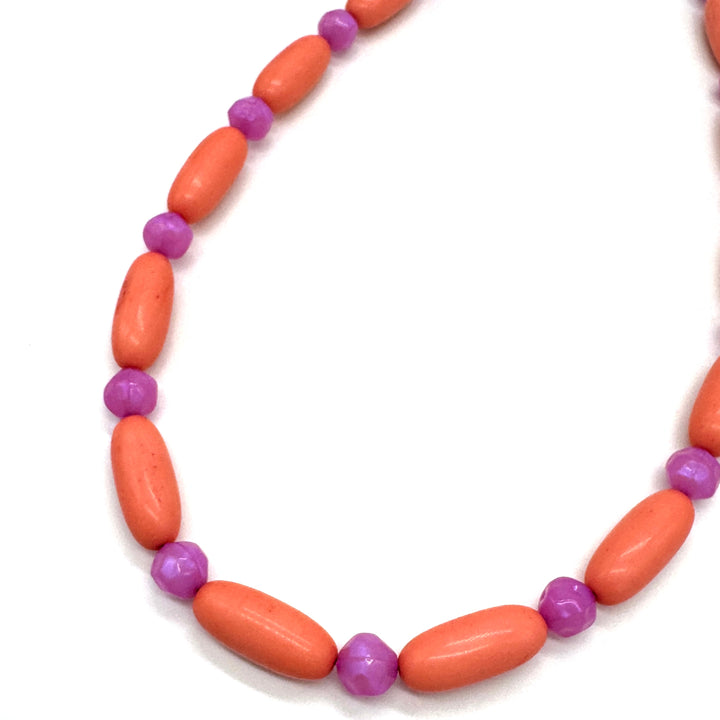 Close up of bright coral and pink beaded necklace on a white background.