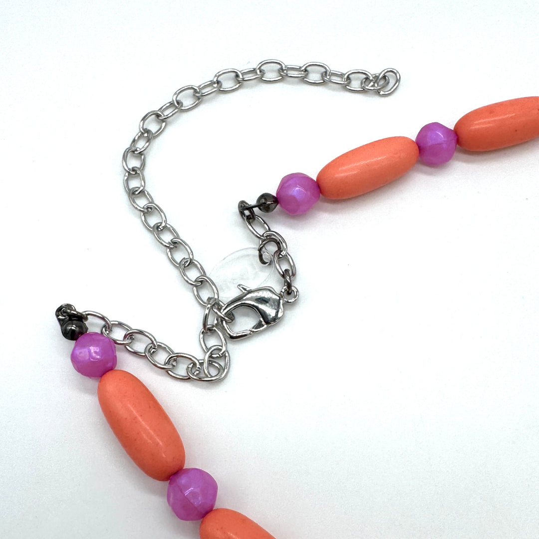 Close up of bright coral and pink beaded necklace's adjustable clasp on a white background.