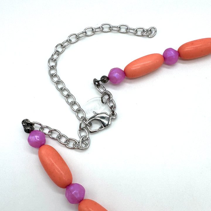 Close up of bright coral and pink beaded necklace's adjustable clasp on a white background.