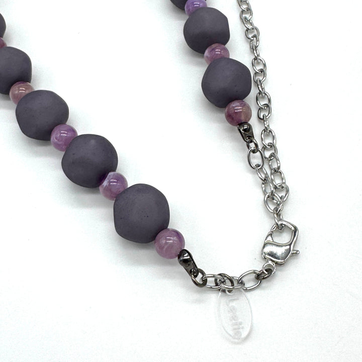Closeup of adjustable necklace featuring dark gray and lilac lucite beads laid on a white background.