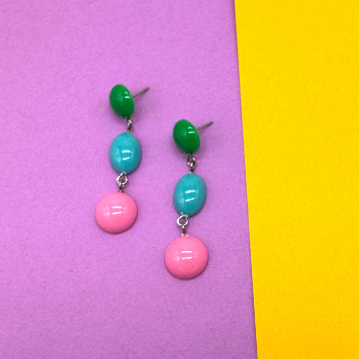Pair of earrings with green, blue, and pink beads on a purple and yellow background