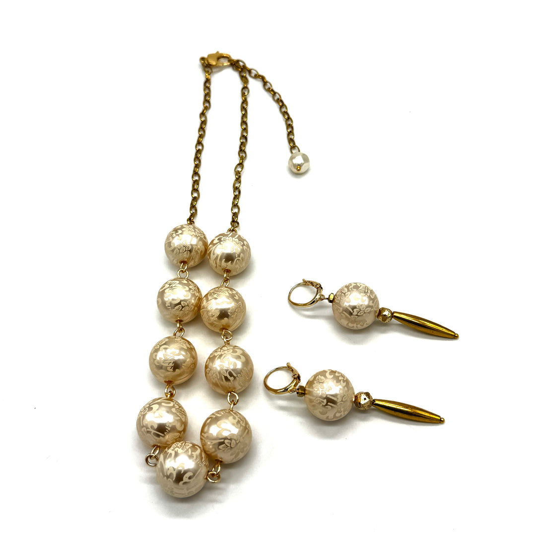 Dangle earrings with floral cream colored beads and golden accents with matching necklace on a white background.