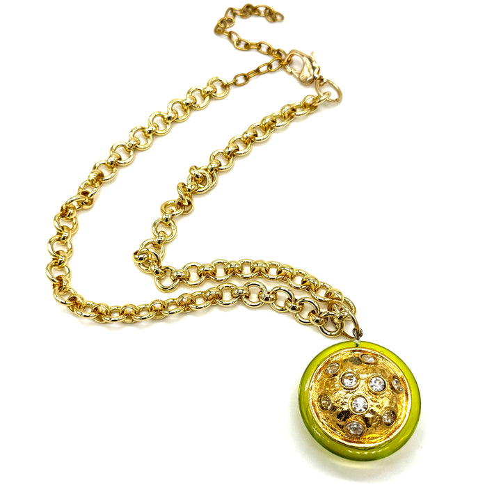 A gold chain necklace featuring a round pendant with a bright lime green outer ring and a textured gold center decorated with small clear rhinestones.