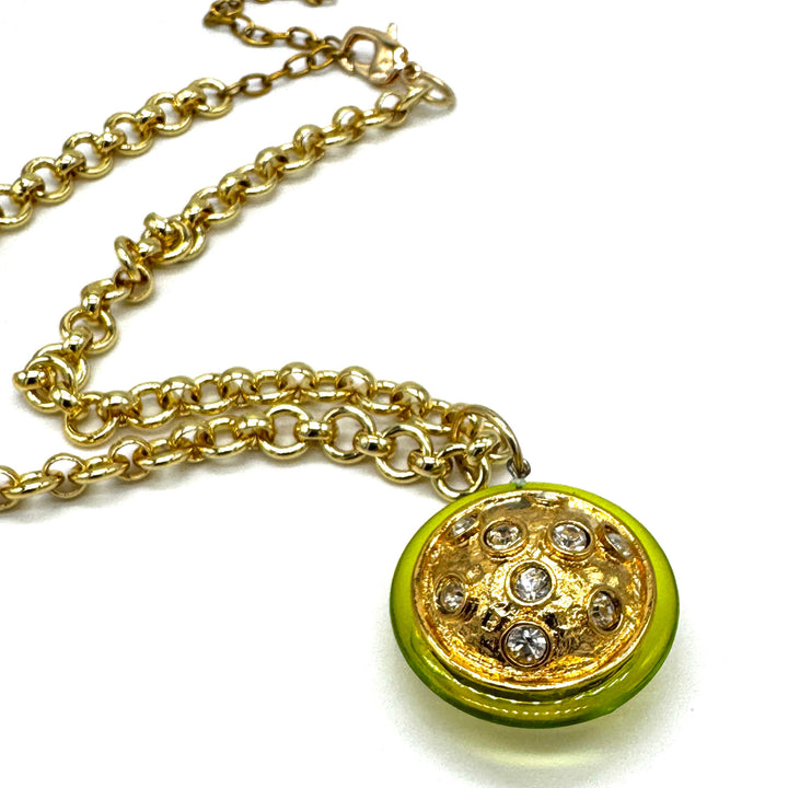 A gold chain necklace featuring a round pendant with a bright lime green outer ring and a textured gold center decorated with clear rhinestones.