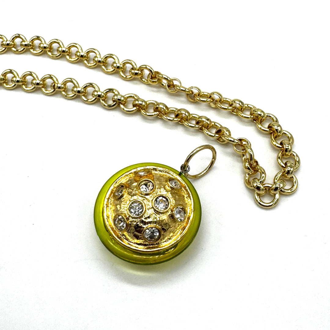 A gold chain necklace with a round pendant featuring a bright yellow-green border and a gold-toned center set with clear rhinestones, shown on a plain white background.