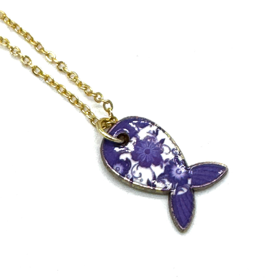 A gold chain necklace featuring a fish-shaped pendant with a purple and white floral pattern, shown on a plain white background.