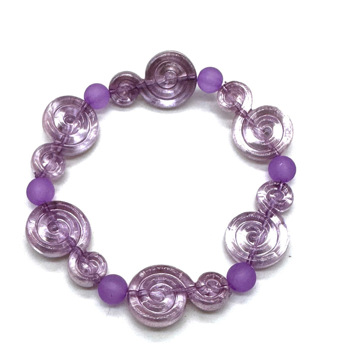 A purple beaded stretch bracelet featuring translucent spiral-shaped beads and smooth round purple beads, displayed on a clean white background.