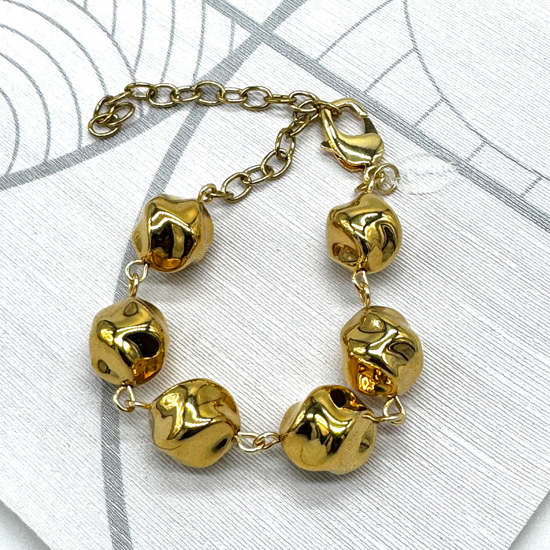 A gold-tone chain bracelet with six irregular, textured bead-like links, displayed on a light gray patterned surface.