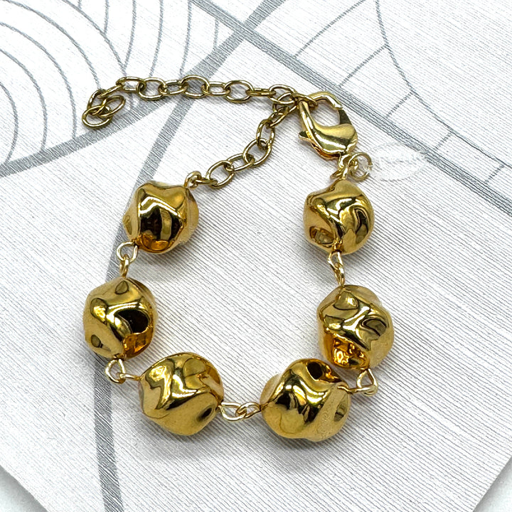 A gold-tone chain bracelet with six irregular, textured bead-like links, displayed on a light gray patterned surface.