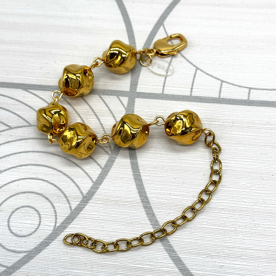 A gold-toned metal bracelet featuring textured, rounded beads and a matching chain extender, displayed on a white background with a gray circular graphic pattern.