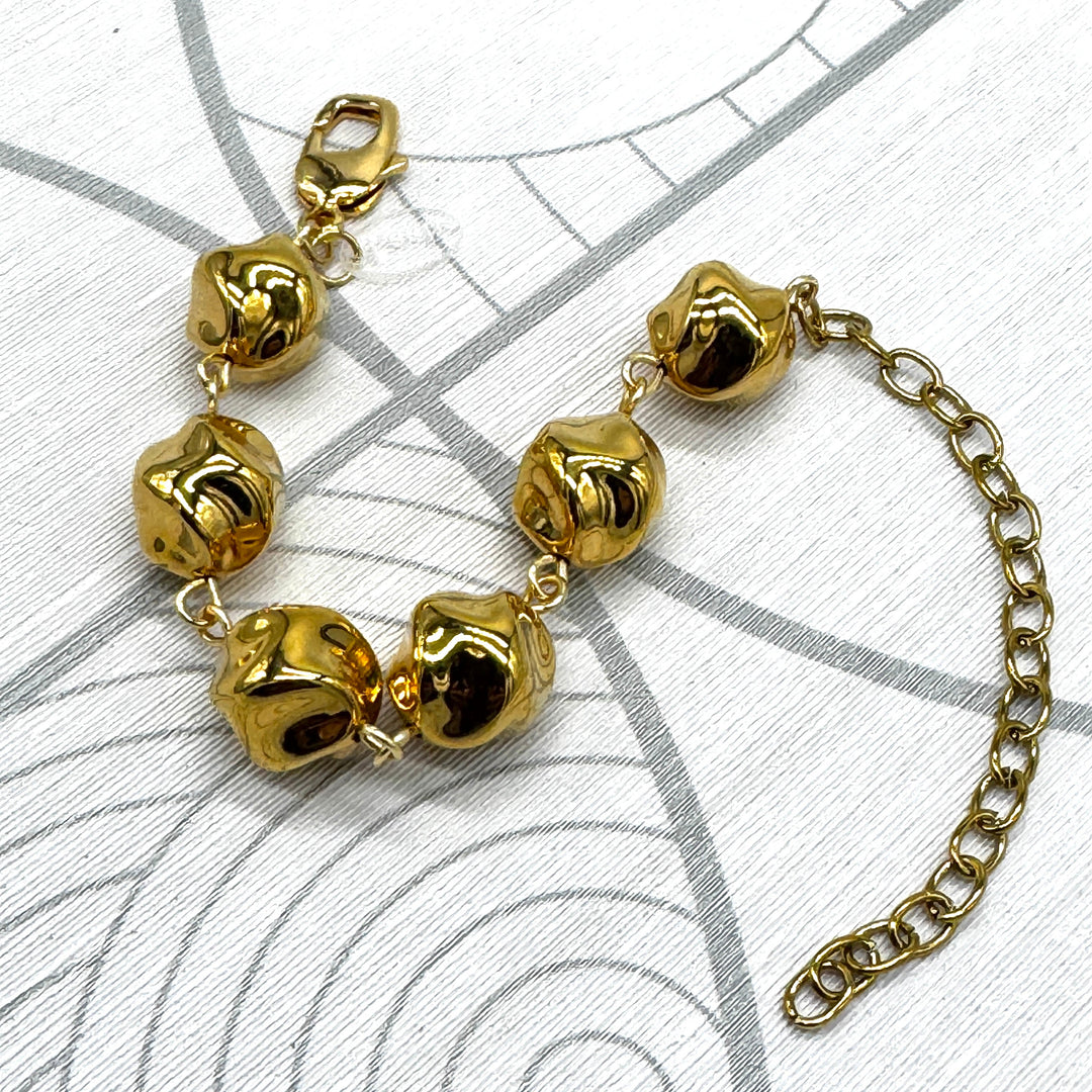 A gold-tone metal bracelet featuring textured, polished twisted round-shaped beads connected by small links, with a lobster clasp on one end and an adjustable extension chain on the other, displayed on a white patterned surface.