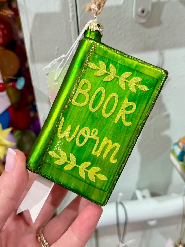 Green ornament with 'Book worm' text held by a hand against a blurred background