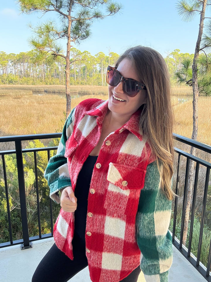 Woman wearing a red and green checkered vest on a balcony with a natural landscape view.