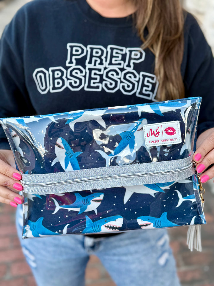 Model holding Makeup Junkie Bags large clear zip pouch in navy shark print with silver glitter zipper while wearing Prep Obsessed sweatshirt outdoors