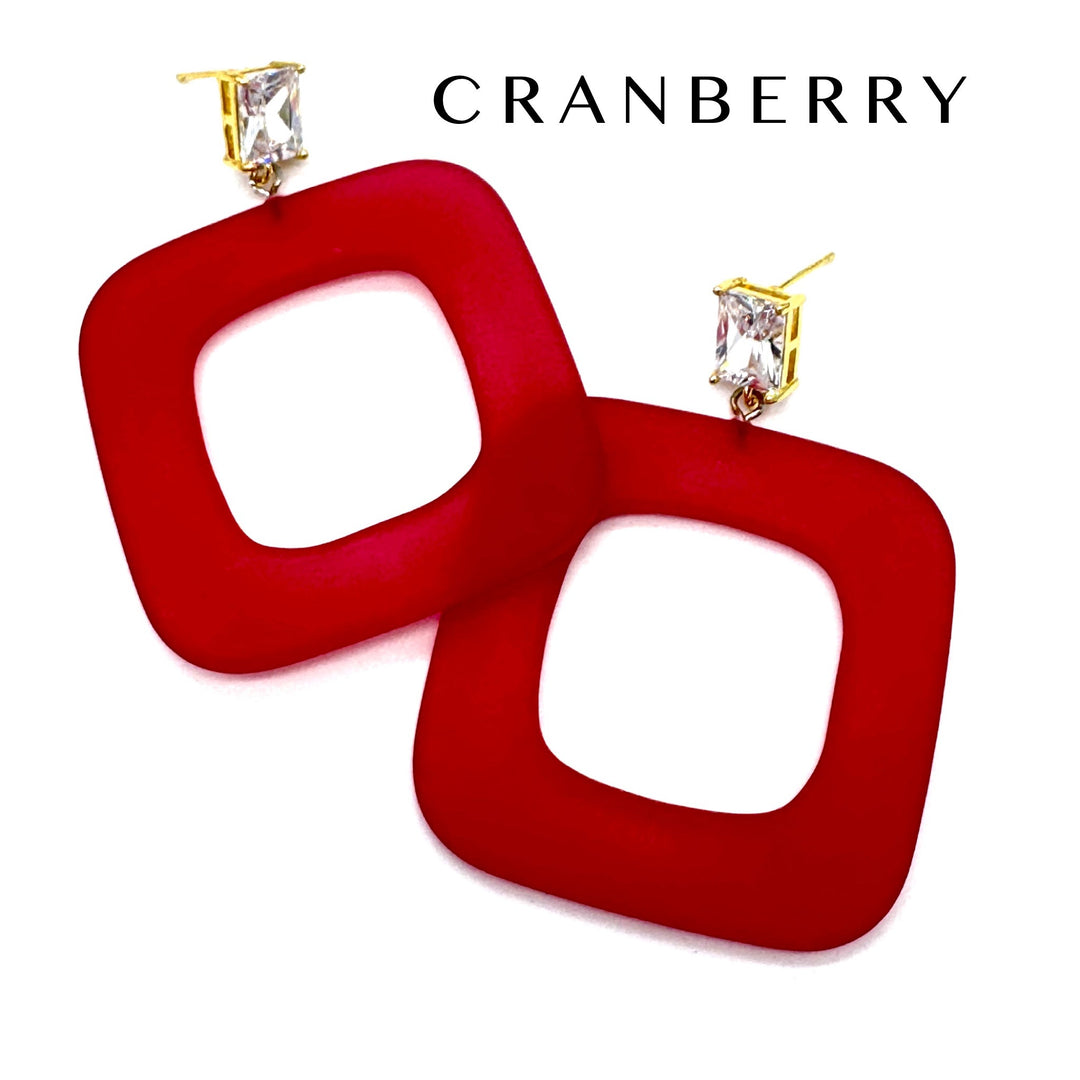 A pair of red square open-frame drop earrings with gold post settings and clear rectangular crystals, shown on a white background with the brand name CRANBERRY at the top.