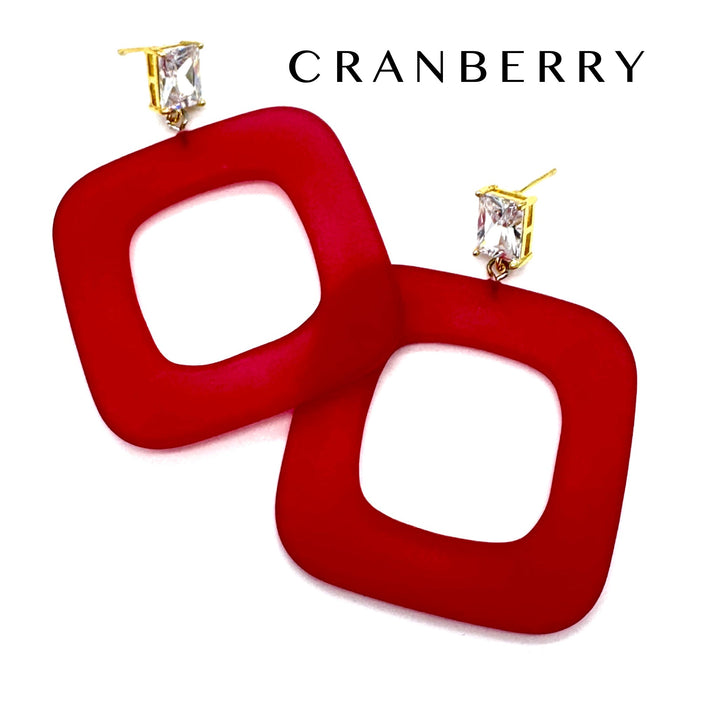 A pair of red square open-frame drop earrings with gold post settings and clear rectangular crystals, shown on a white background with the brand name CRANBERRY at the top.