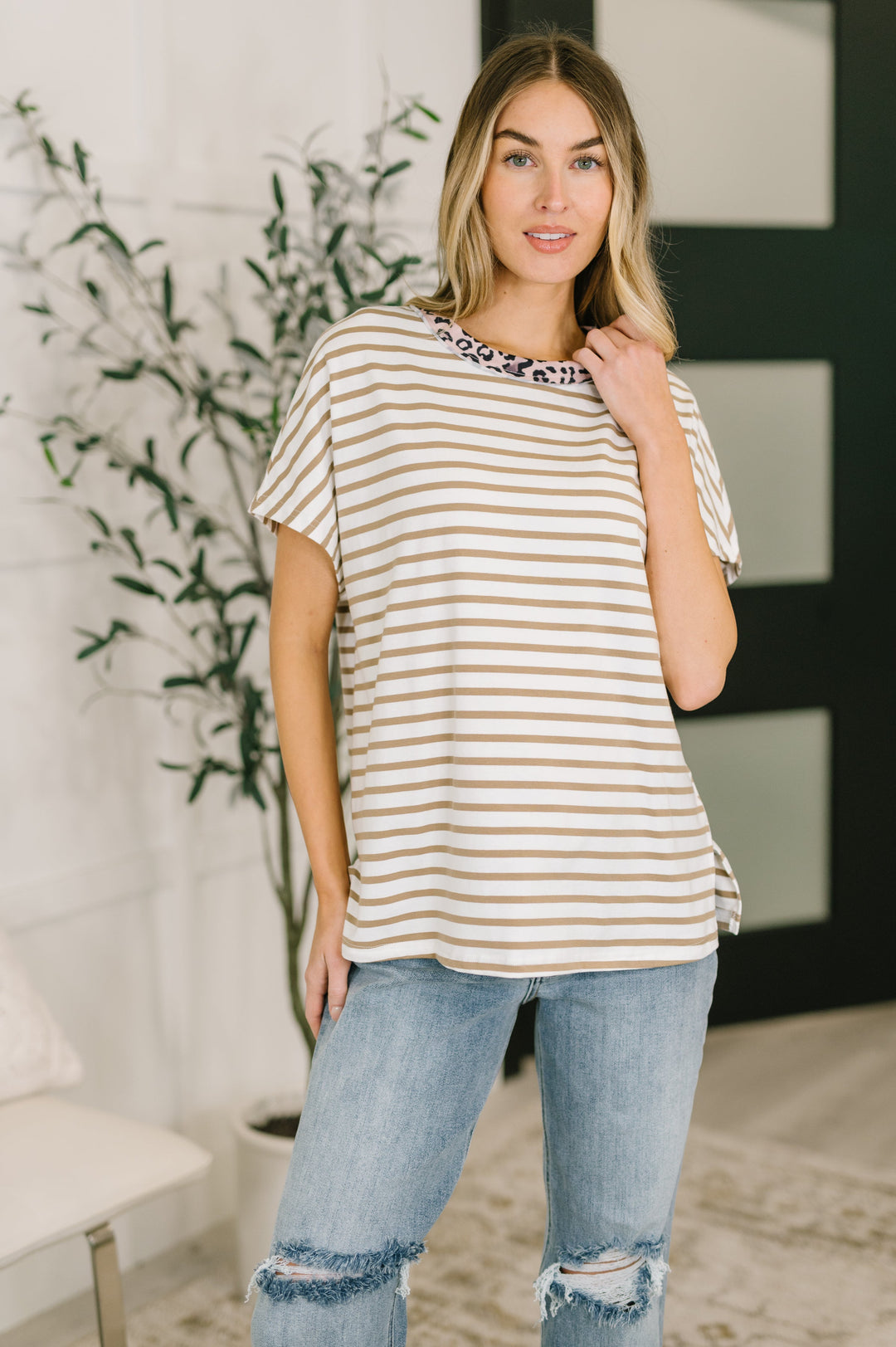 Woman wearing a white and tan striped oversized tee with pink leopard print neckline trim, styled with distressed light wash jeans.