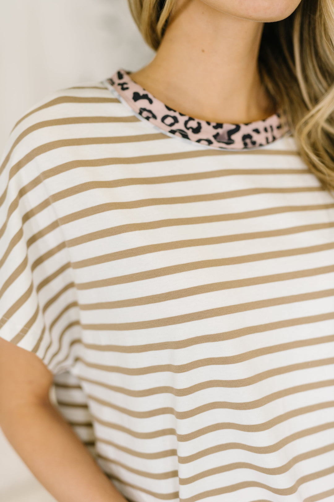 Close-up of white and tan striped oversized tee showing pink leopard print crew neckline trim detail.
