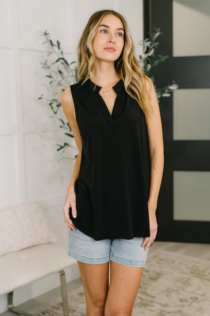 Woman in a black sleeveless split-neck top paired with light wash denim shorts and a gold necklace.