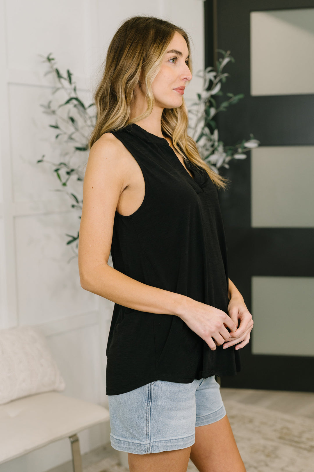 Side view of a woman in a black sleeveless split-neck top and wide-leg jeans.