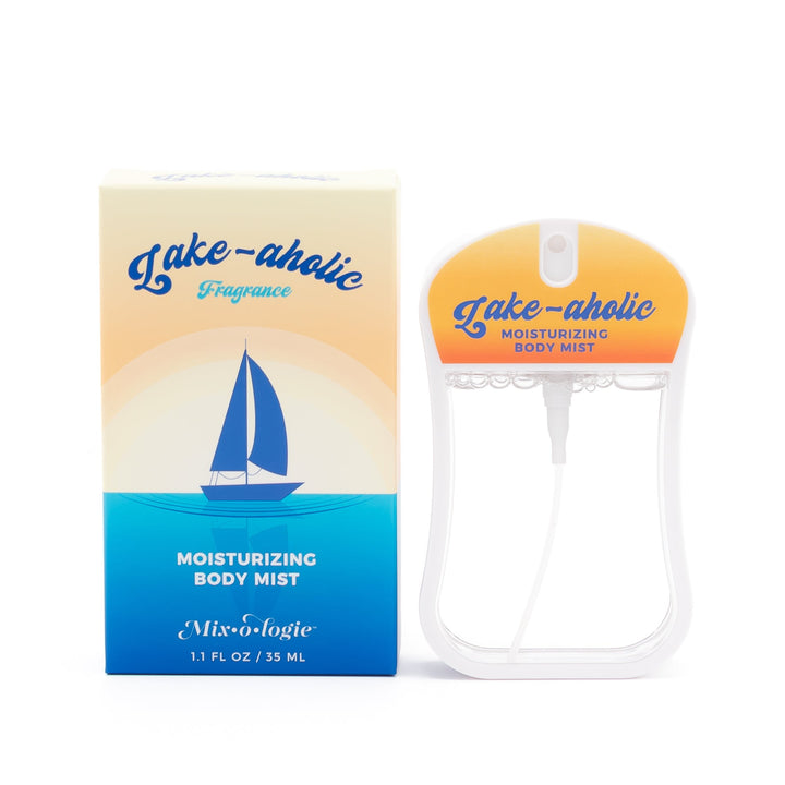Mixologie Moisturizing Body Mist in Lake-aholic, 1.1 fl oz, clear card-shaped spray bottle with yellow to orange sunset gradient cap next to cream and blue sailboat illustration box on white background