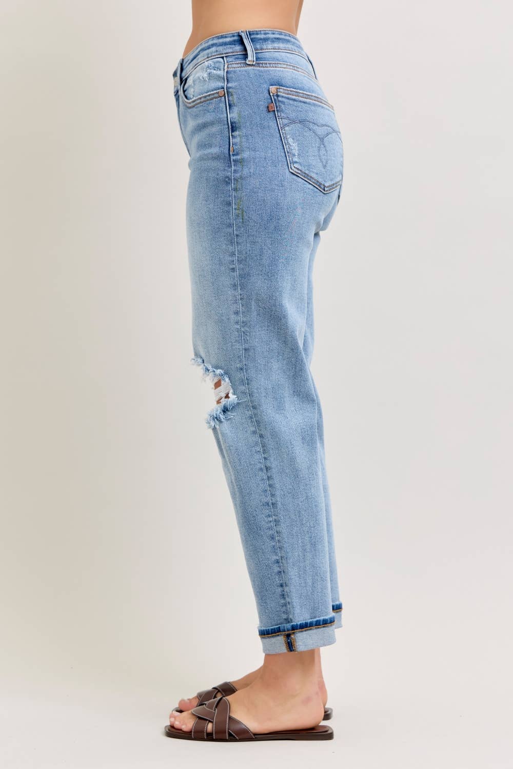 Side view of light wash distressed straight-leg jeans with frayed knee cutout and cuffed hem in plus size paired with brown woven slide sandals
