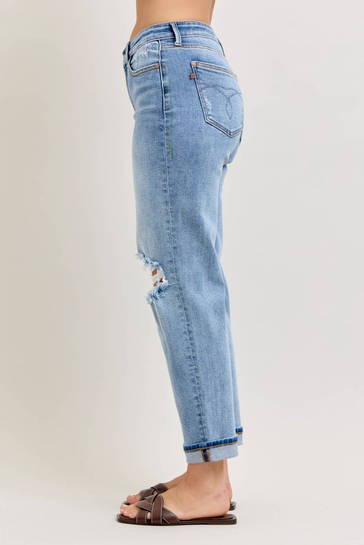 Side view of light wash distressed straight-leg jeans with frayed knee cutout and cuffed hem in plus size paired with brown woven slide sandals
