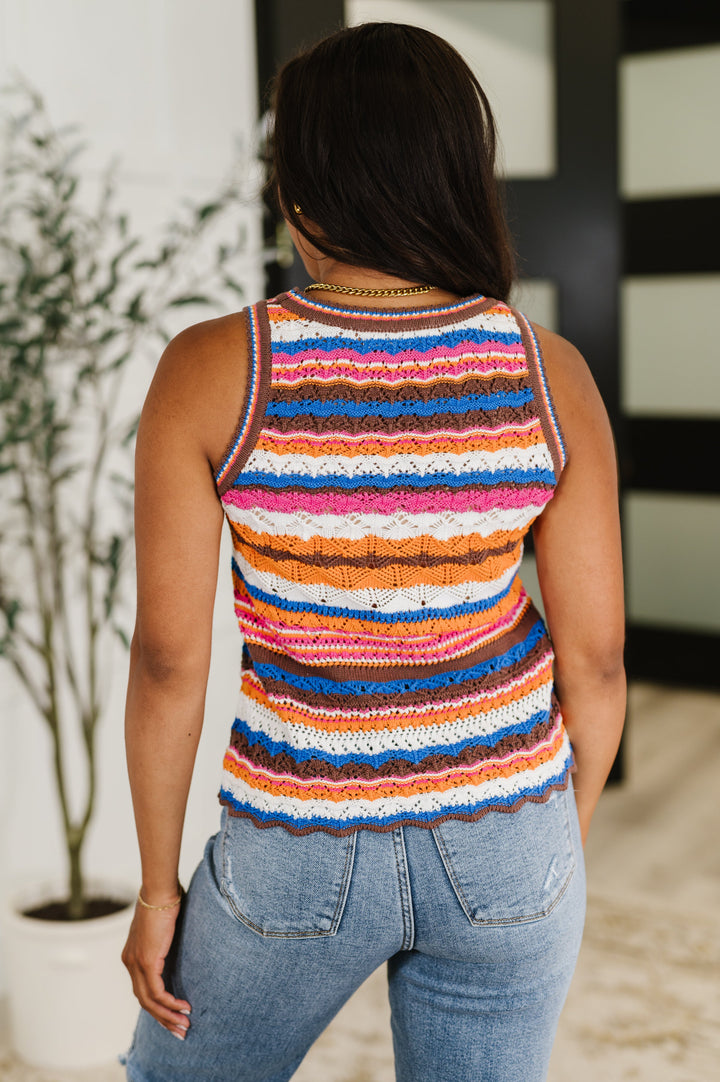 Back view of a woman in a multicolor striped crochet knit tank top and jeans.