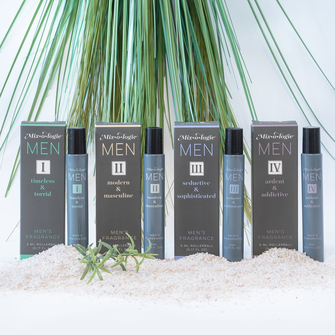 Mixologie Men's Fragrance collection, four 5 ml rollerballs — I Timeless & Torrid, II Modern & Masculine, III Seductive & Sophisticated, and IV Ardent & Addictive — each with matching box displayed in white sand with tall green palm grass in background