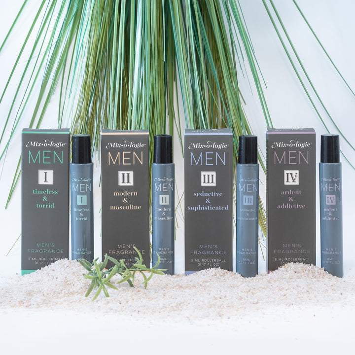 Mixologie Men's Fragrance collection, four 5 ml rollerballs — I Timeless & Torrid, II Modern & Masculine, III Seductive & Sophisticated, and IV Ardent & Addictive — each with matching box displayed in white sand with tall green palm grass in background