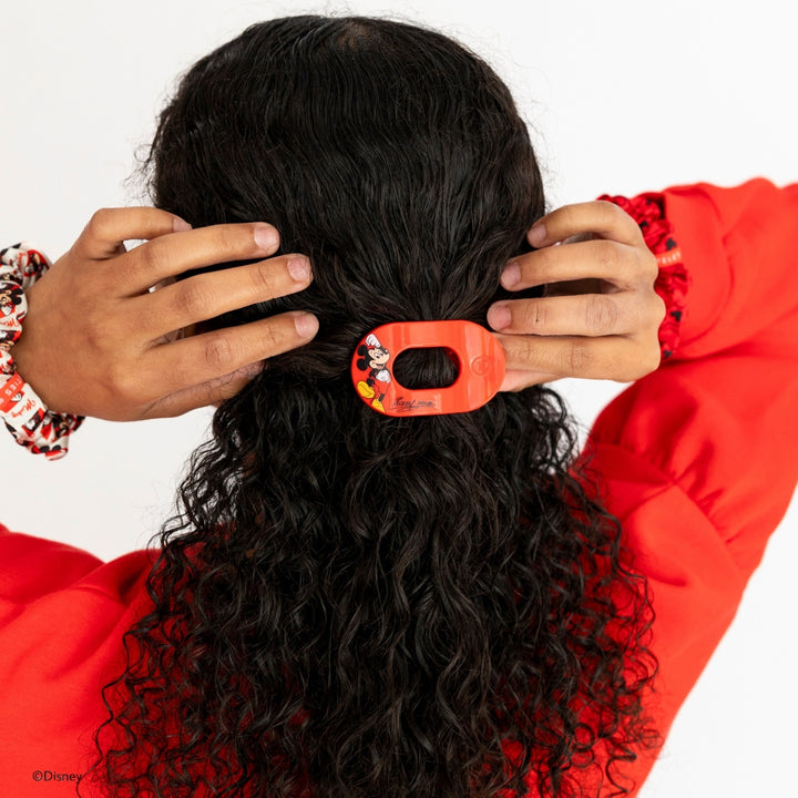 Disney x Teleties Mickey Mouse small flat round hair clip in red being placed in half-down style on curly dark hair by model in red sweatshirt against white background