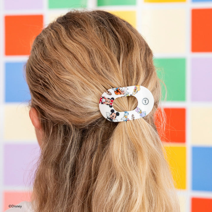 Disney x Teleties Mickey and Friends tiny flat round hair clip in white with allover character print securing a low ponytail on blonde hair against colorful grid background